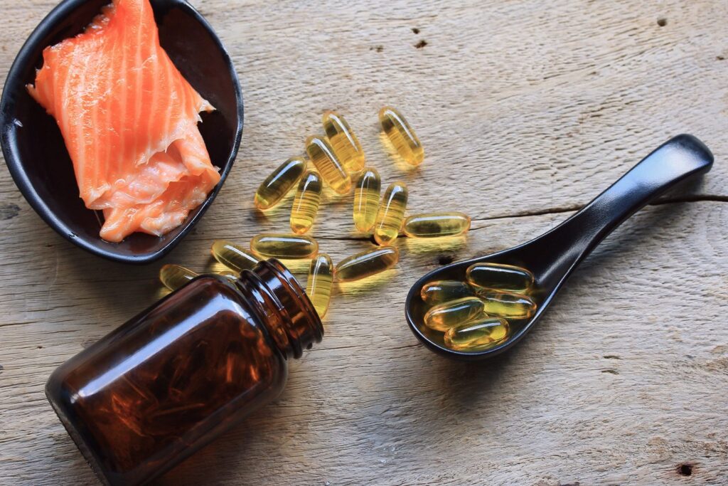 Omega-3 softgel capsules spilling from an amber bottle beside a fresh salmon fillet