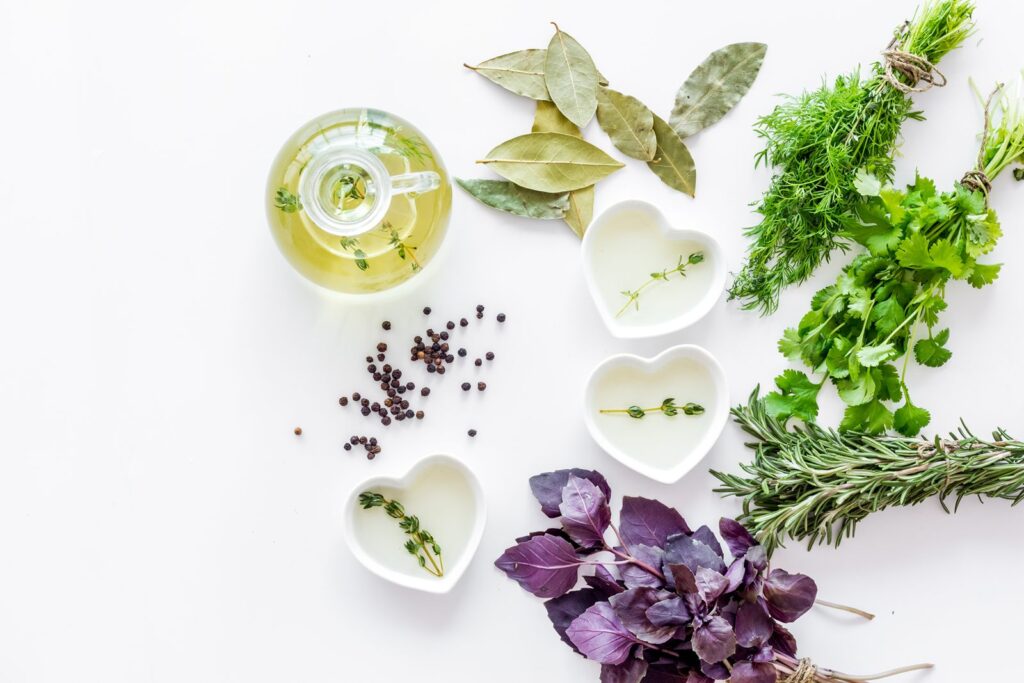 Fresh herbs, peppercorns and small dishes of herbal oil laid out on a white surface