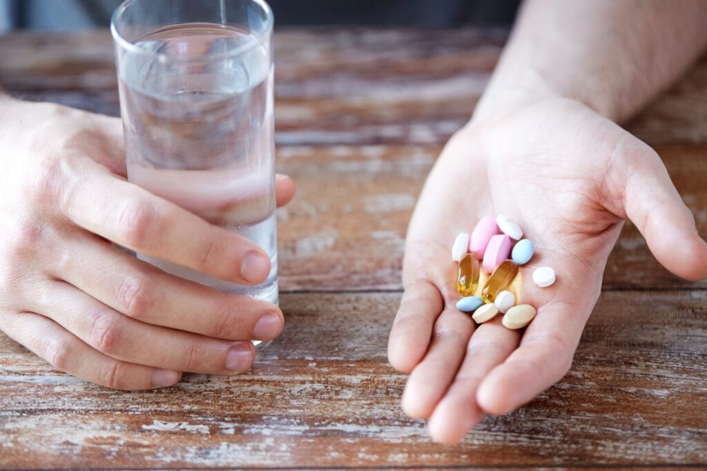 Hands holding an assortment of mineral supplement tablets beside a glass of water